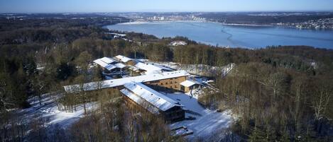 An aerial view of a building complex surrounded by snow-covered trees and a river.