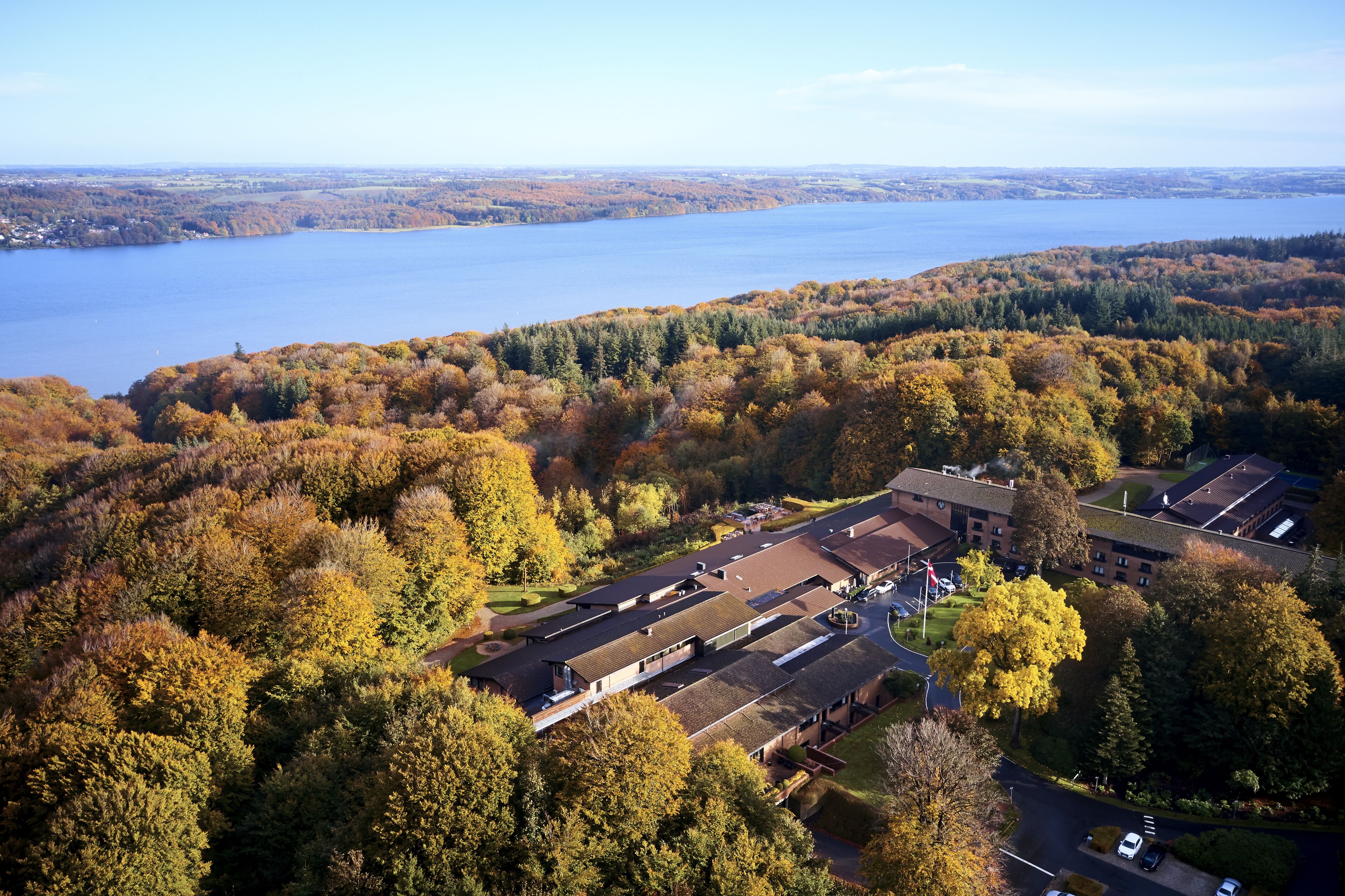 An aerial view of a building surrounded by autumn foliage and a lake.