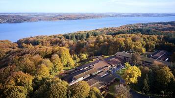 An aerial view of a building surrounded by autumn foliage and a lake.