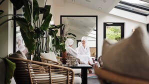 Un interior moderno con mobiliario de mimbre, plantas grandes en macetas y vistas al verdor exterior.