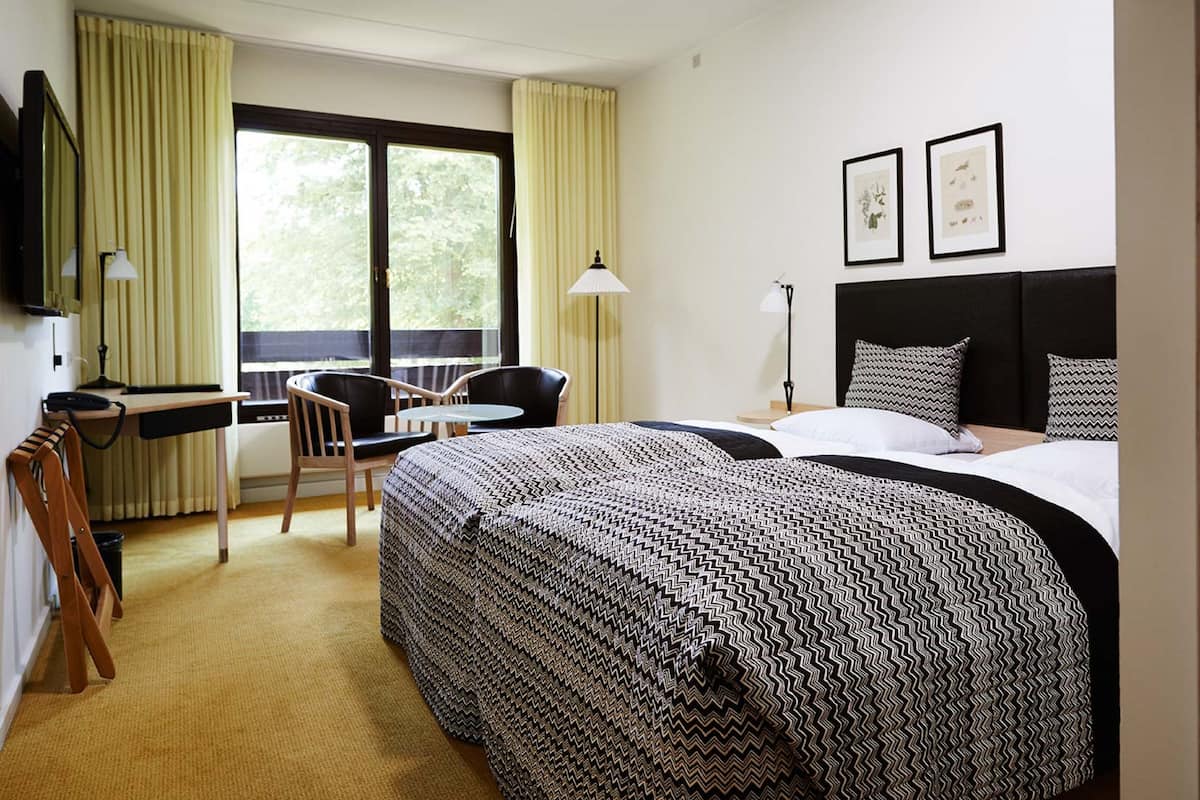 Ein Hotelzimmer mit einem großen Bett, einem Schreibtisch, einem Sessel und einem Fenster mit Vorhängen.