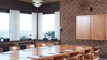 A conference room with a long wooden table, brown leather chairs, a brick wall, and a large window with curtains.