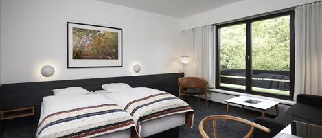 A hotel room with two beds, a desk, a chair, a window with curtains, and a framed picture on the wall.
