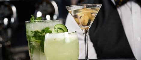 Two cocktails on a tray, one with mint and cucumber, and the other with lemon slices.