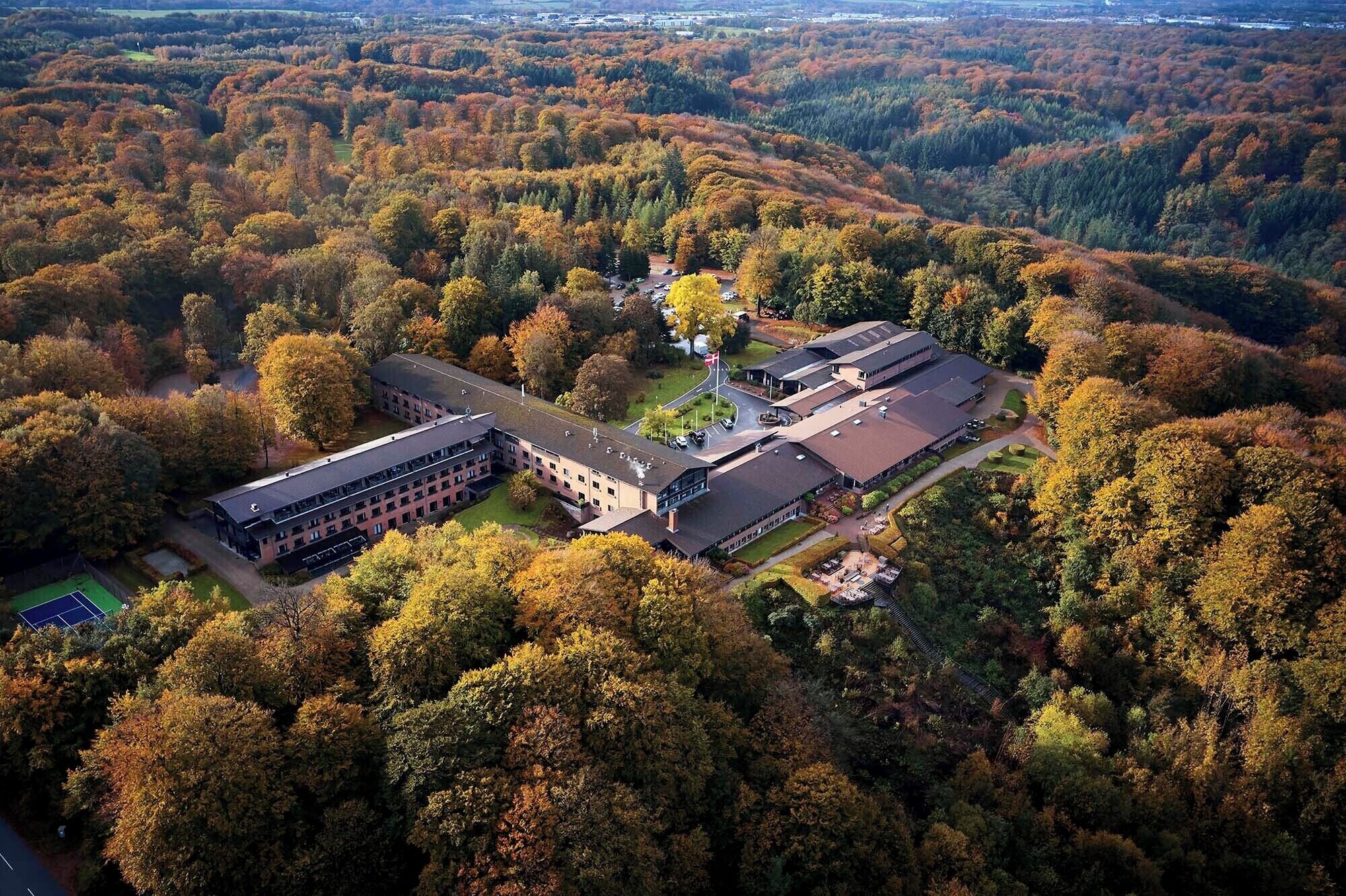 An aerial view of a campus with multiple buildings surrounded by dense forest.