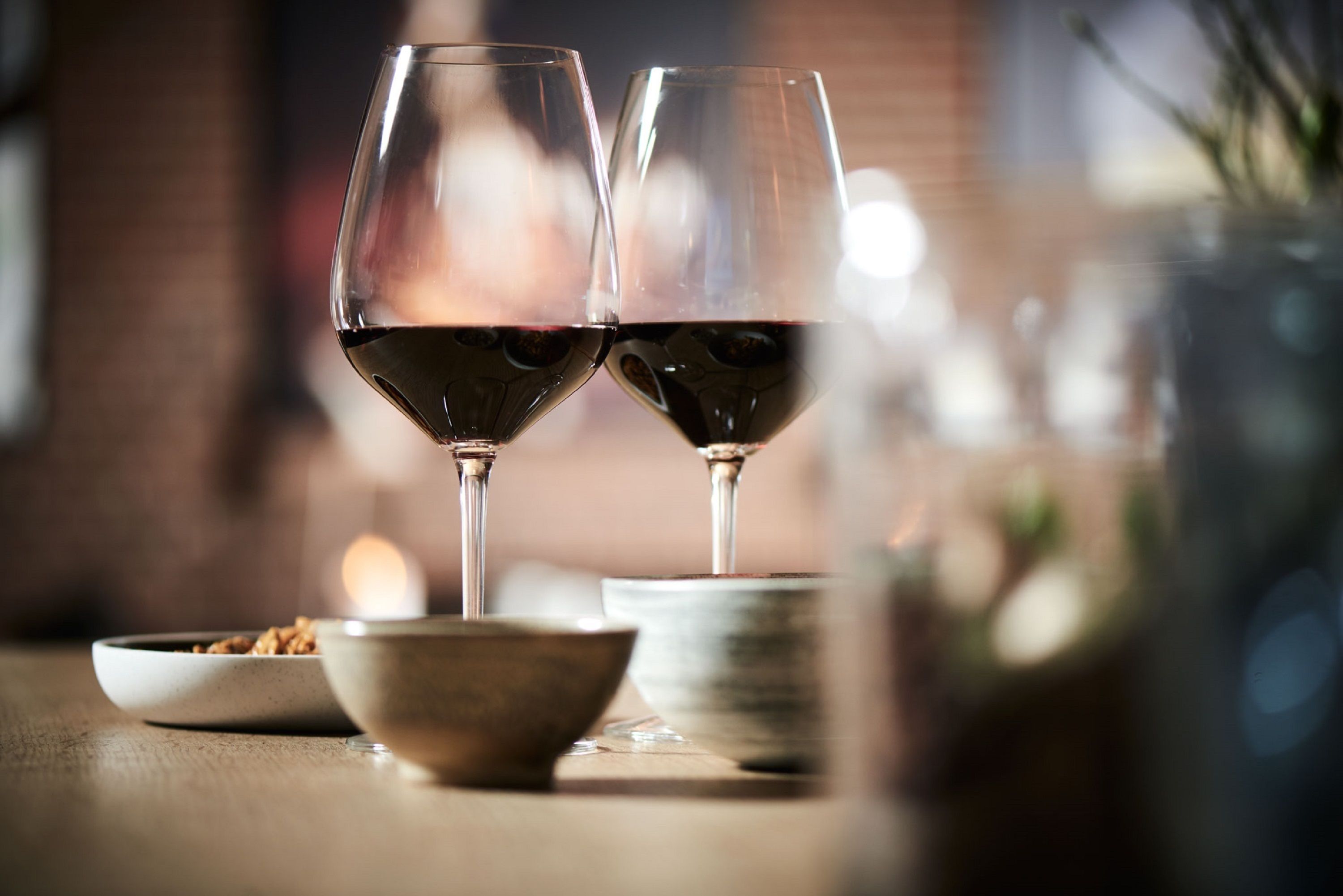 Dos copas de vino sobre una mesa, con un frutero y una vela al fondo.