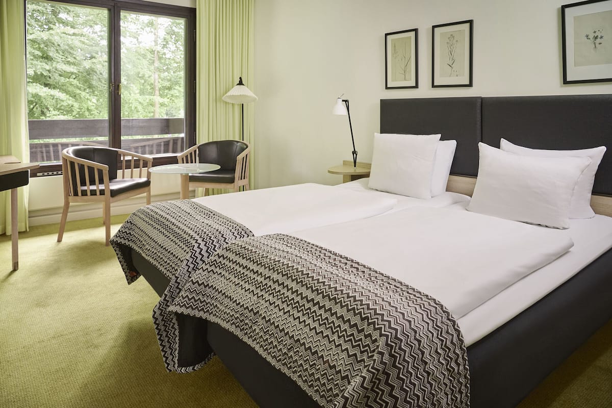 Ein Hotelzimmer mit einem großen Bett, einem Schreibtisch mit Stuhl, einer Lampe und gerahmten Bildern an der Wand.