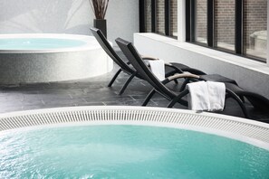 A modern indoor pool area with lounge chairs and a hot tub.