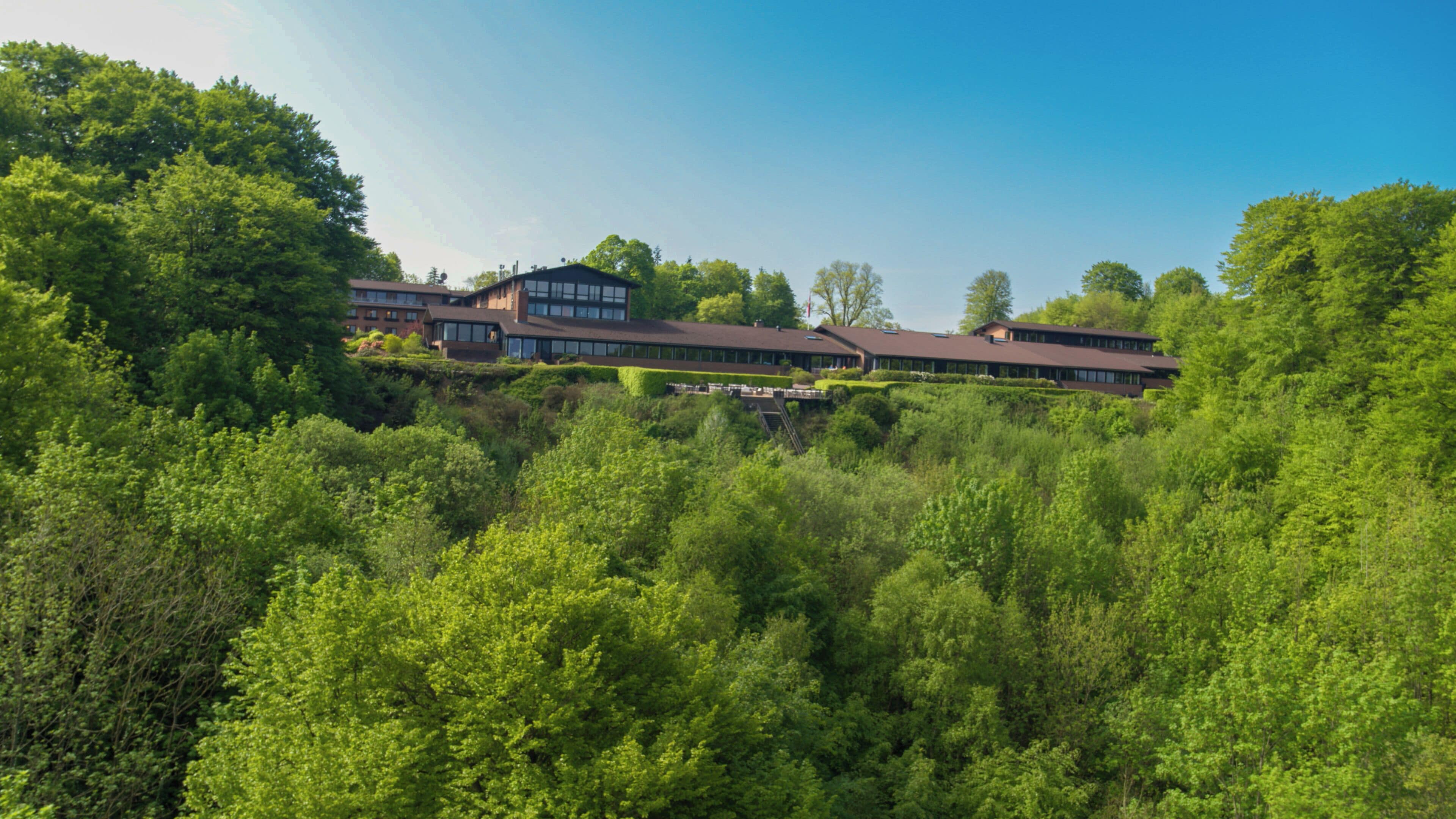 A modern building with a flat roof, surrounded by dense green foliage.