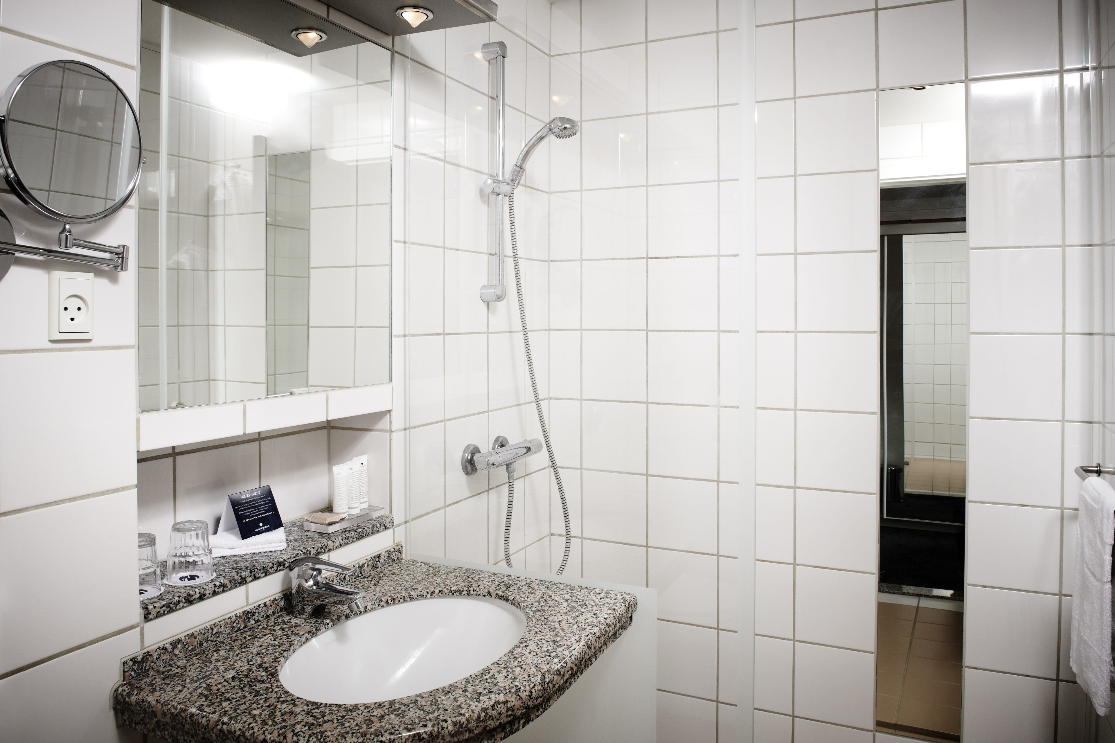 Een badkamer met een granieten wastafel, een spiegel, een handdouche en een handdoekhouder.