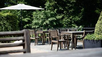 Un patio al aire libre con mesas y sillas de madera, rodeado de exuberante follaje.