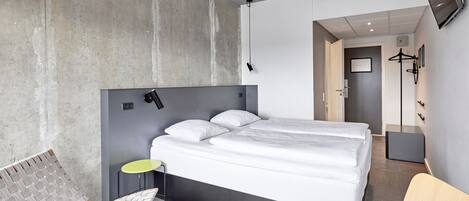 A modern hotel room with a large bed, a small table, a chair, and a TV mounted on the wall.