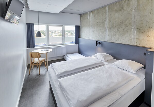 Habitación de hotel con dos camas, una silla, una mesa y un ventanal grande.