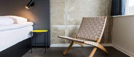 A hotel room with a bed, a small table, a chair, and a wall-mounted light.