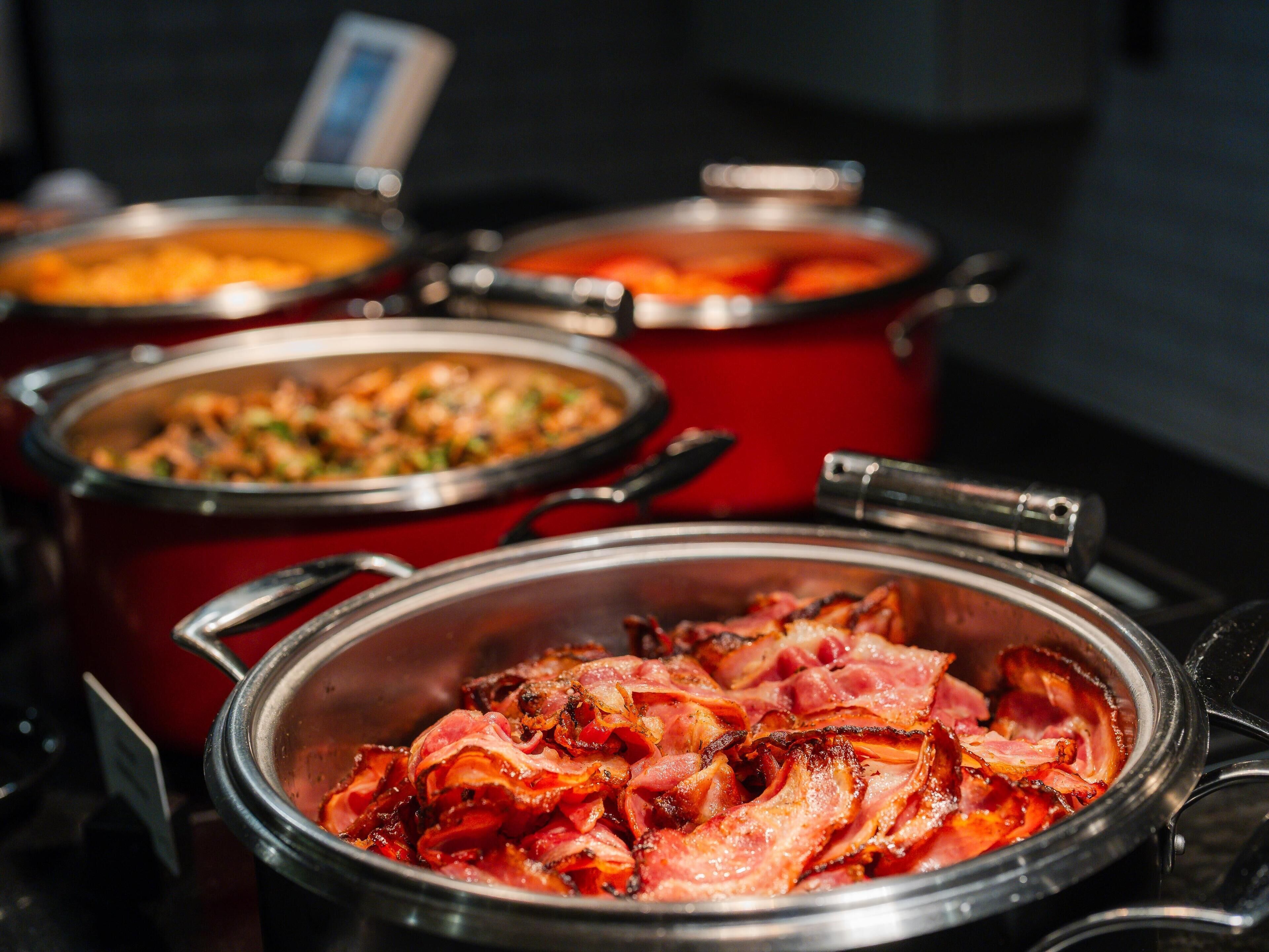A buffet with various dishes, including a prominent container of bacon.