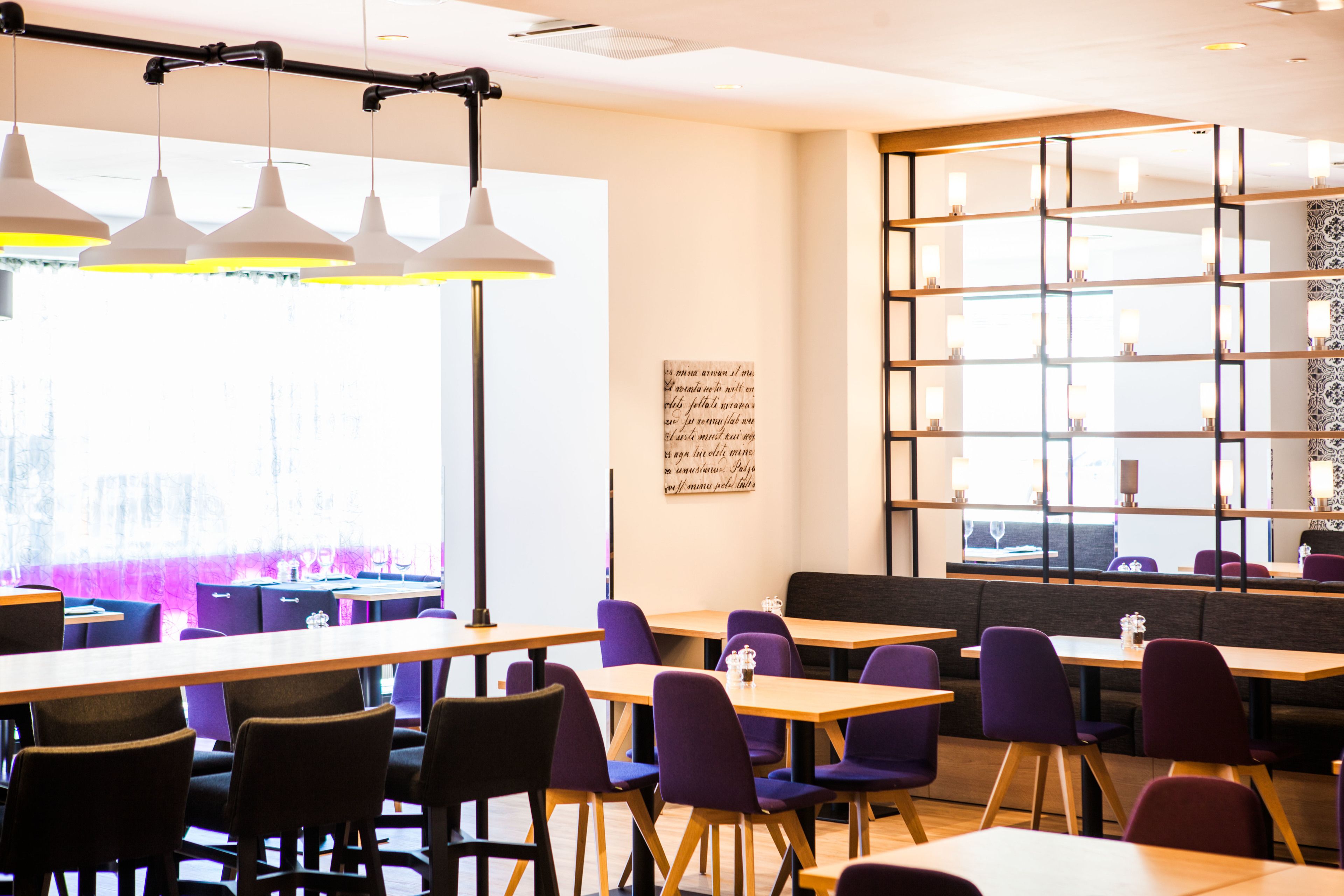 A modern restaurant with wooden tables and purple chairs, large windows, and pendant lighting.