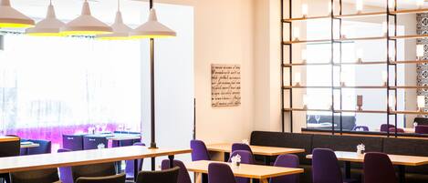 A modern restaurant with wooden tables and purple chairs, large windows, and pendant lighting.