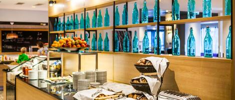 Zona de buffet con diferentes alimentos y una exhibición de botellas de vidrio verde.