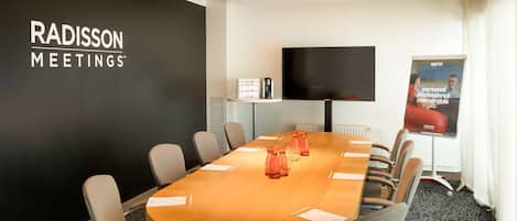 Una sala de conferencias con una mesa larga, sillas, un televisor y un cartel en la pared.