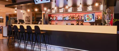 A bar area with a counter, bar stools, a television screen, and a variety of bottles and glasses.