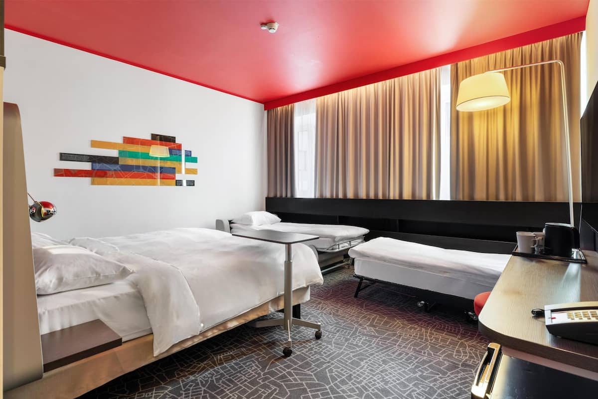 A hotel room with two beds, a desk, a chair, a lamp, and a large window with curtains.