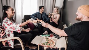 A group of people in a room with a pizza box, a laptop, and a lamp. - Hotel Helka (Helsinki)