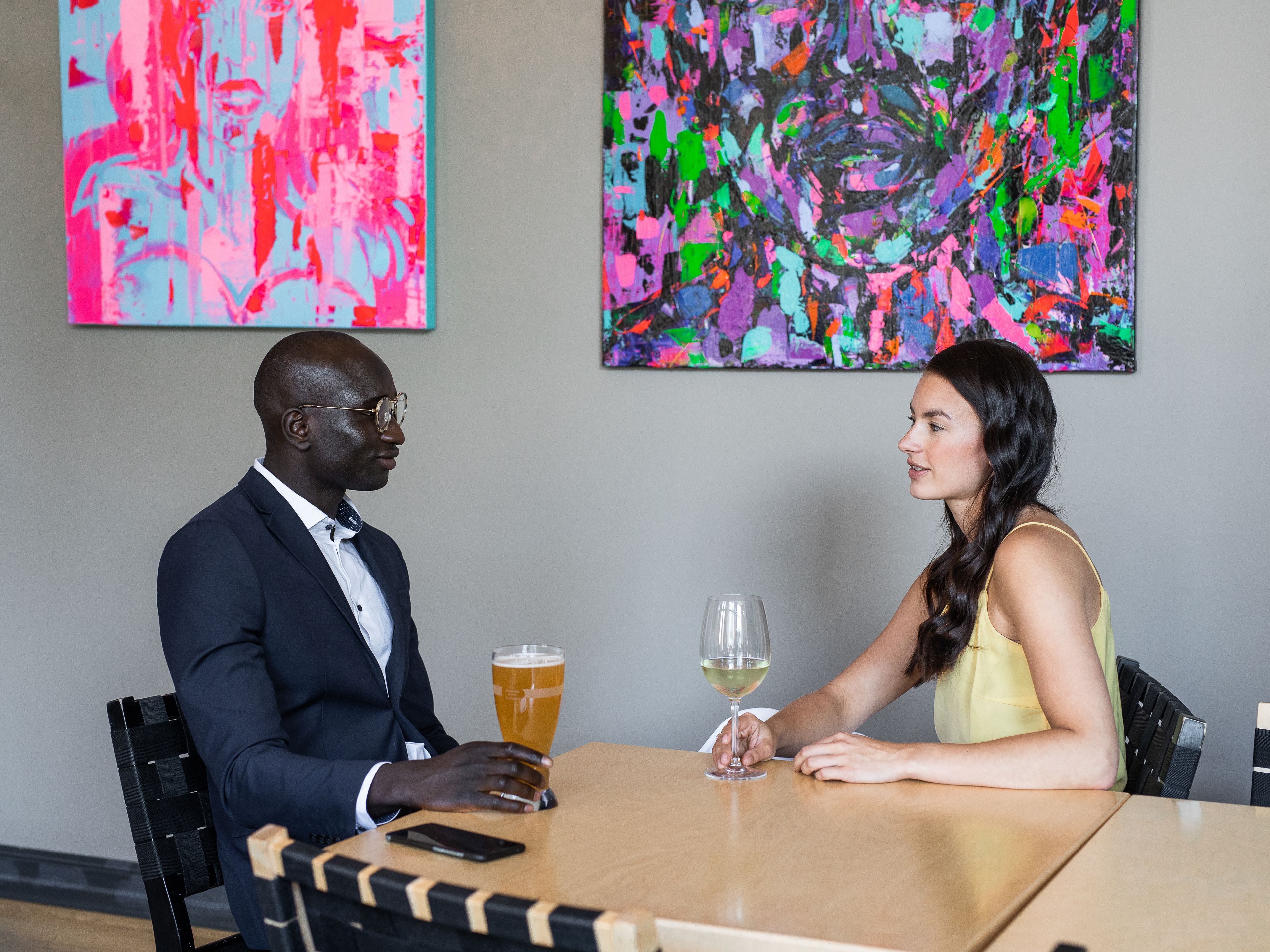 Een man en een vrouw zitten aan een tafel in een kamer met abstracte schilderijen aan de muur.