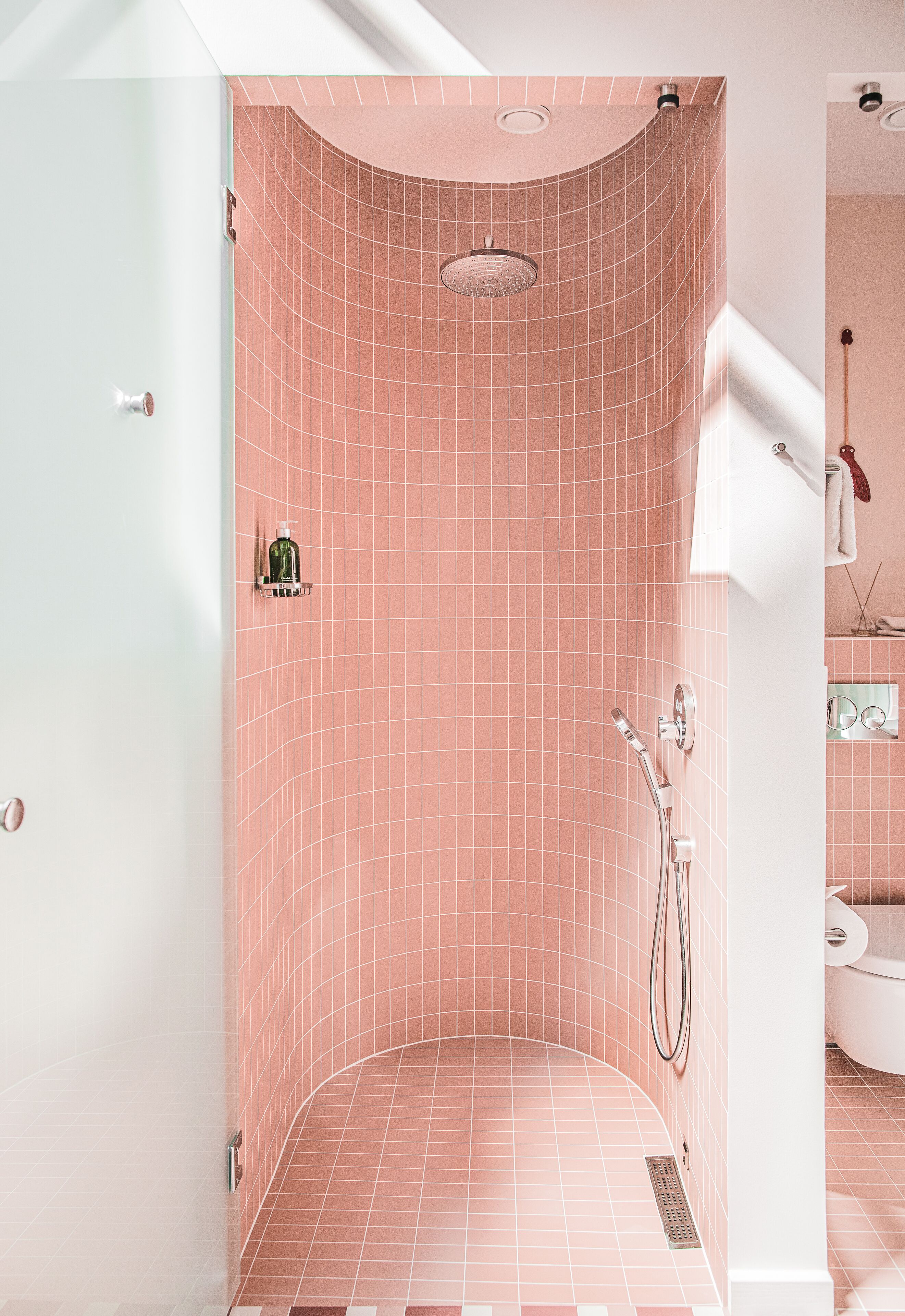 Ducha con azulejos rosas, un cabezal de ducha manual y un grifo instalado en la pared.
