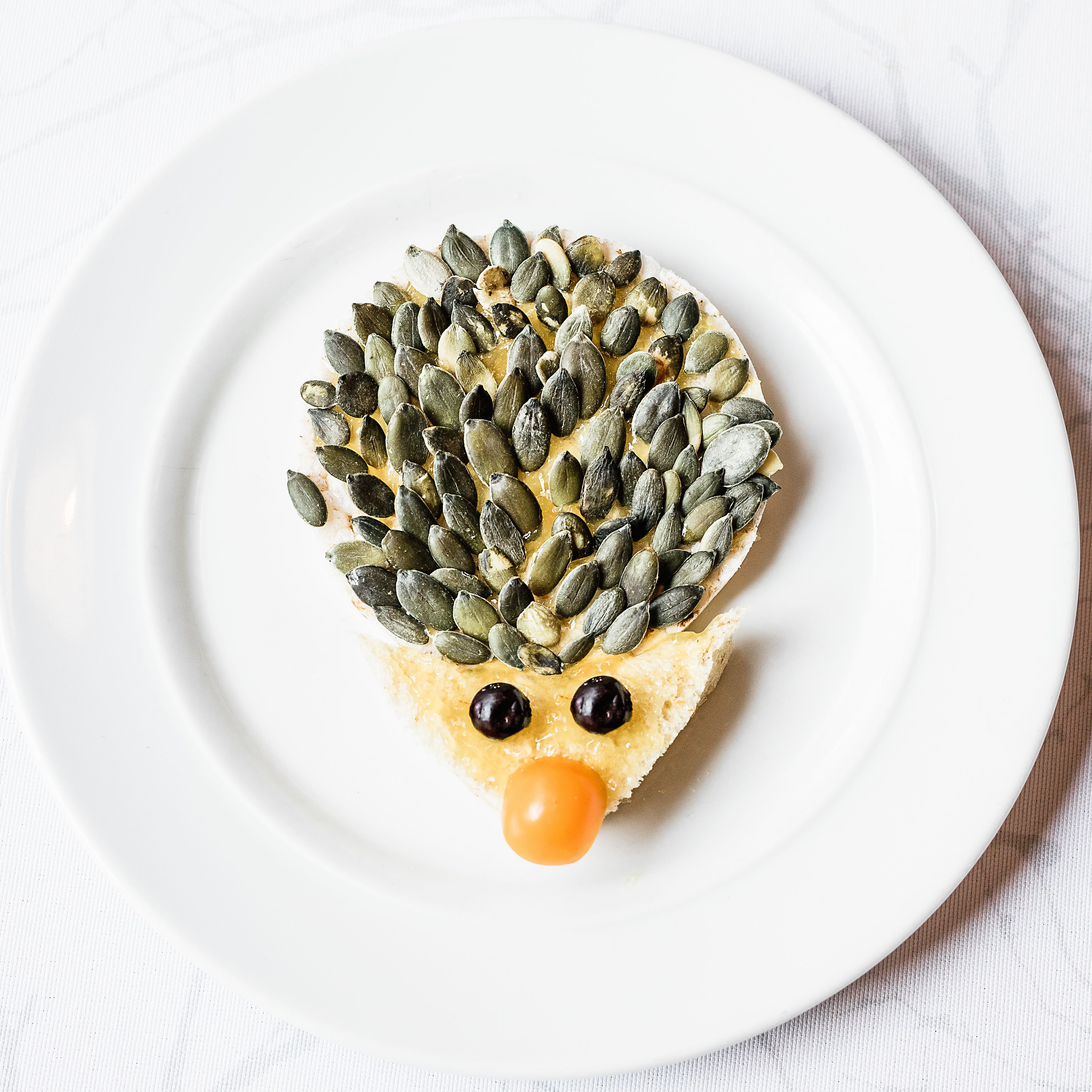 Un plato blanco con un alimento con forma de erizo hecho de semillas y un pequeño trozo naranja.