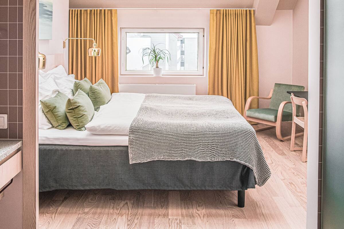 Un dormitorio con tragaluz, una cama con almohadas verdes, una ventana con cortinas y una silla.
