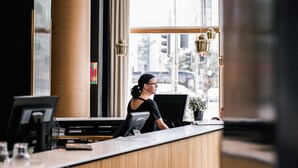 A reception desk with a computer, a plant, and a window with a view of a cityscape. - Hotel Helka (Helsinki)