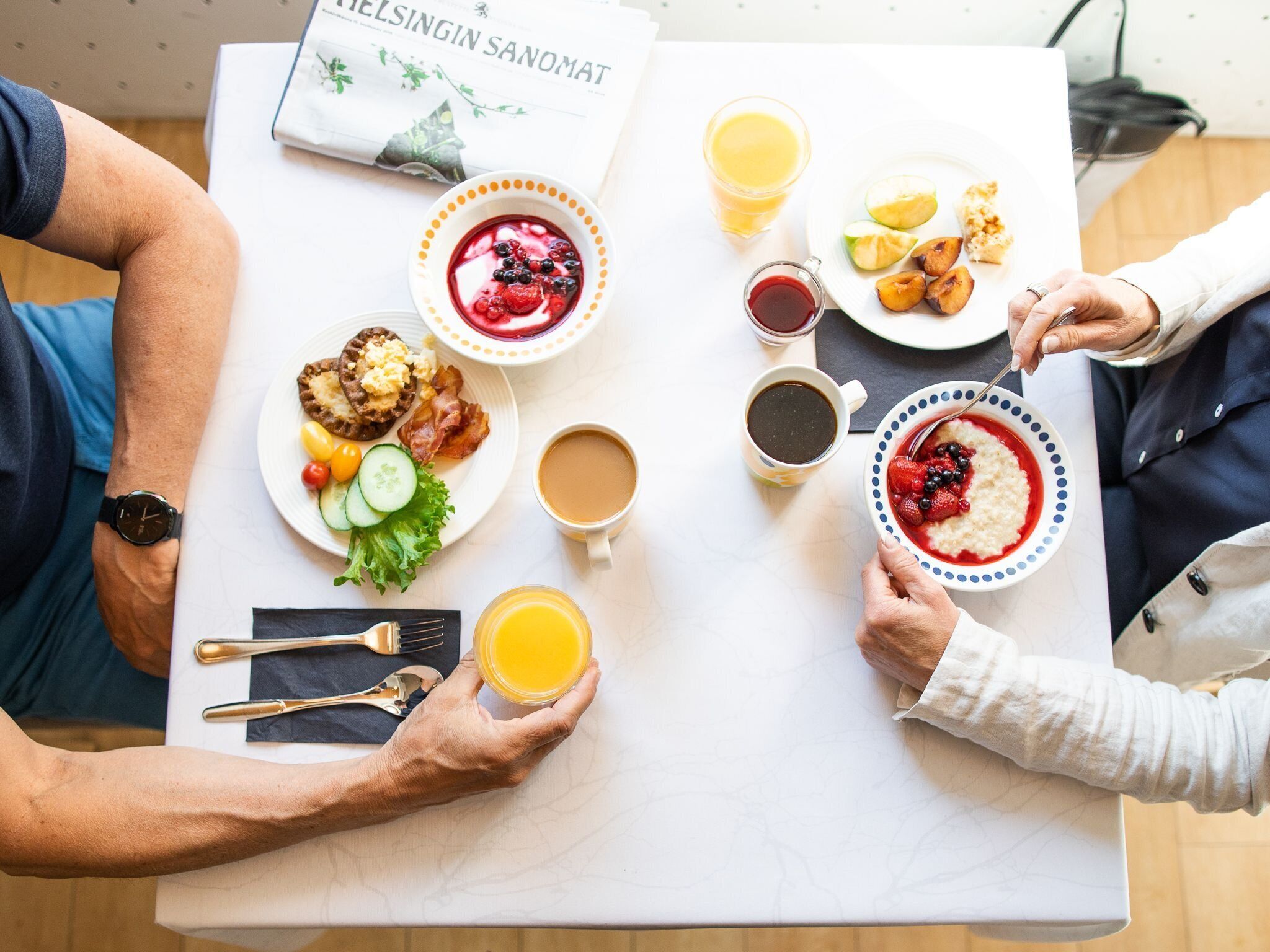 Una mesa de desayuno con diversos platos, bebidas y un libro titulado 'Helsingin Sanomat'.
