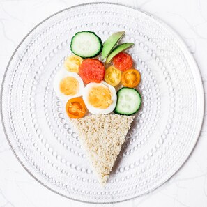 A plate with a slice of bread topped with sliced cucumbers, cherry tomatoes, and boiled eggs.