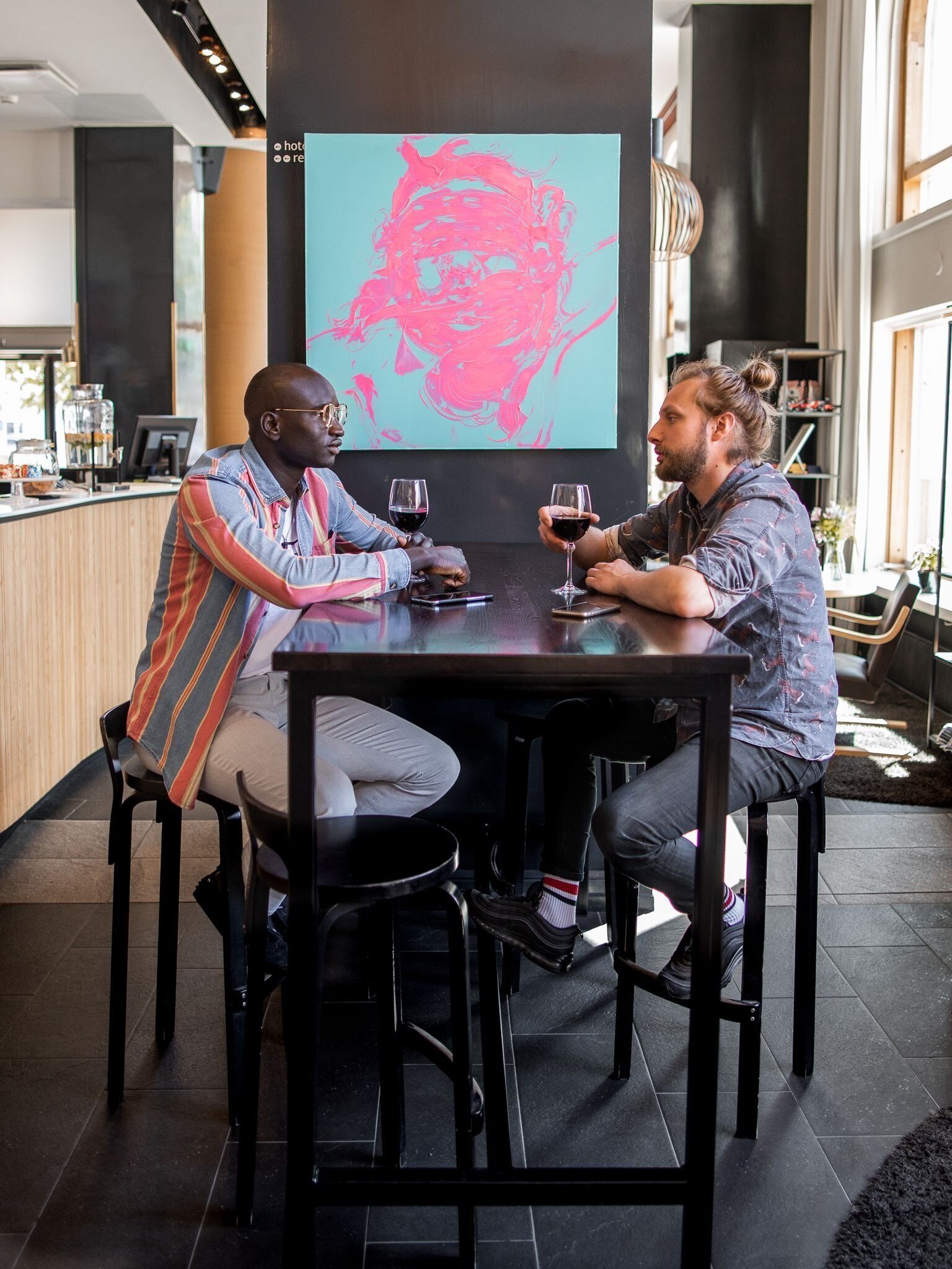 Dos personas sentadas en una mesa con una pantalla grande que muestra una imagen abstracta rosa de fondo.
