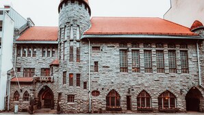 A historic stone building with a tower, arched windows, and a red-tiled roof. - Home Hotel Jugend (Helsinki)