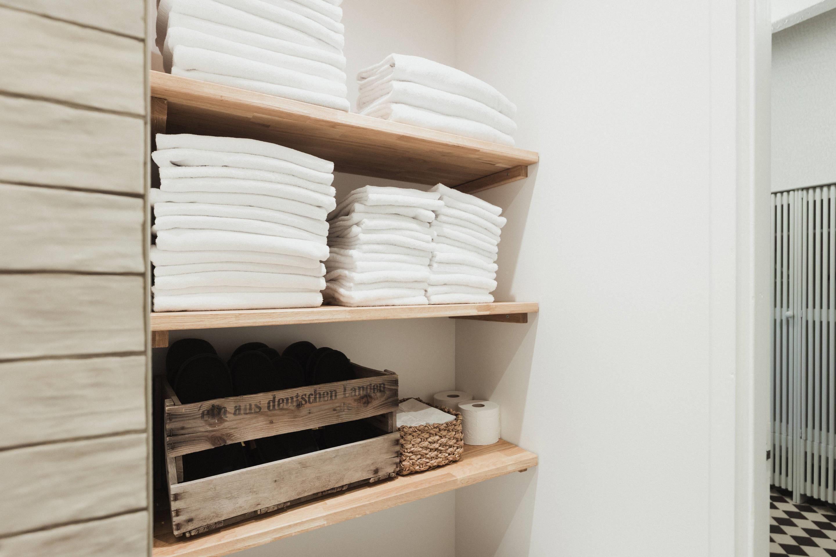 A wooden shelf unit with neatly folded white towels and a wooden crate containing black shoes.