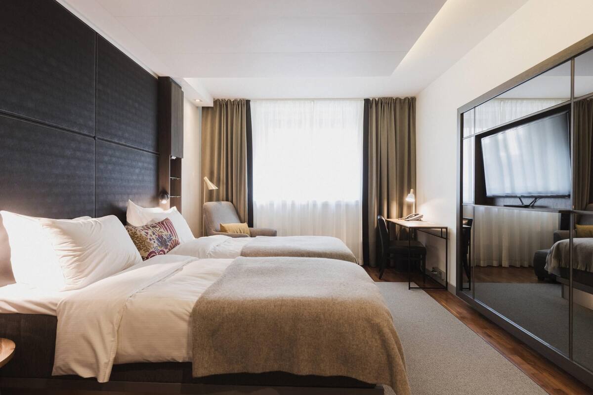 Une chambre d’hôtel avec deux lits, un bureau, une chaise et un grand miroir.