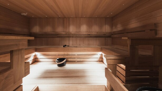 A sauna with wooden benches and a bench with a black bucket. - Home Hotel Jugend (Helsinki)