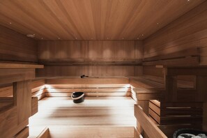 A sauna with wooden benches and a bench with a black bucket. - Home Hotel Jugend (Helsinki)