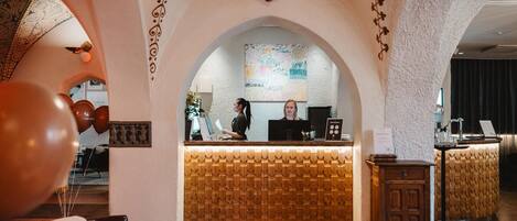 A reception area with a wooden reception desk, a receptionist, and a decorative wall with a floral pattern.