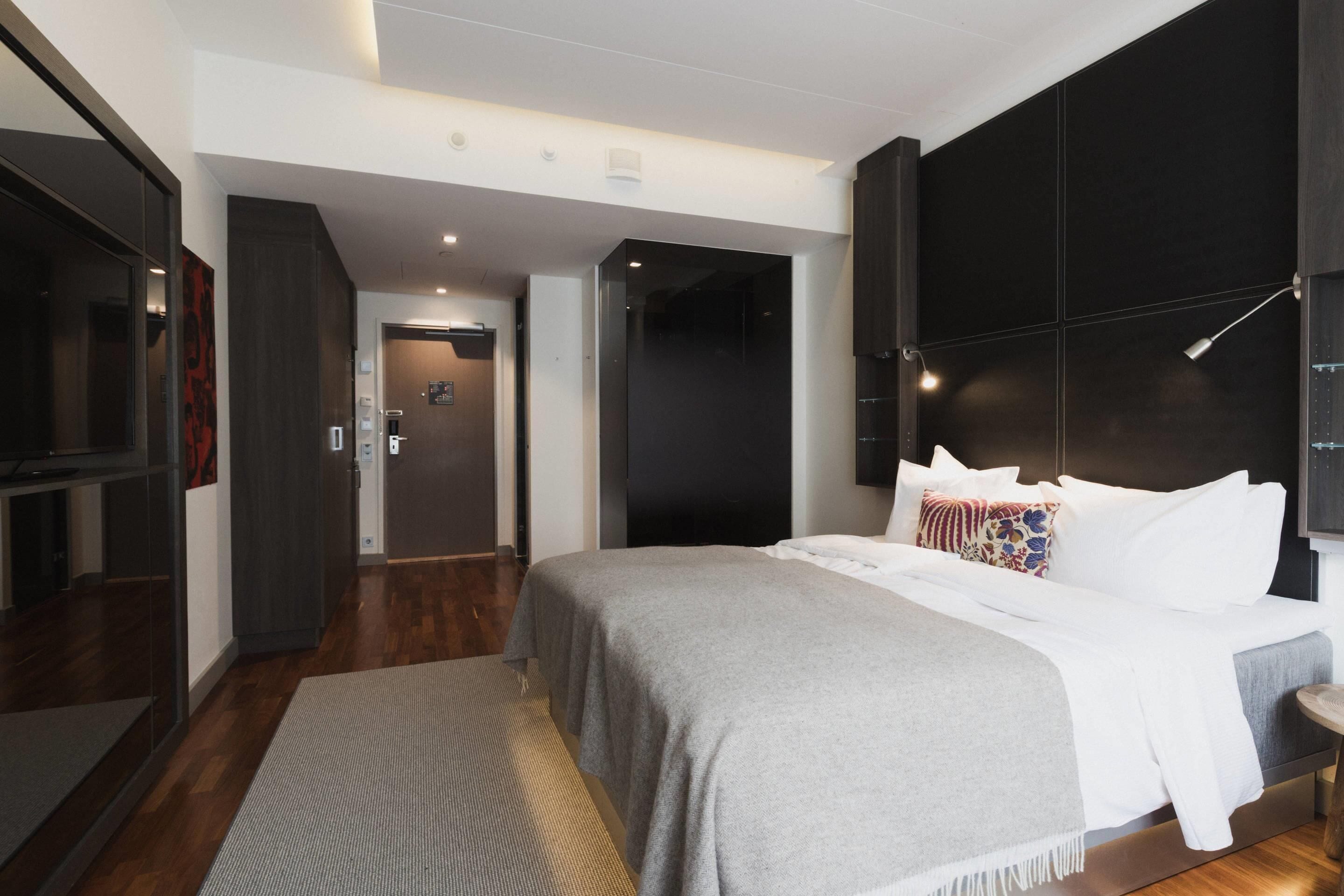 Una moderna camera d'hotel con un letto grande, una testiera scura e un televisore a sinistra.