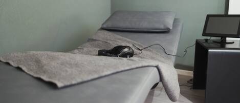 Una habitación con camilla de masaje, auriculares y monitor de ordenador.