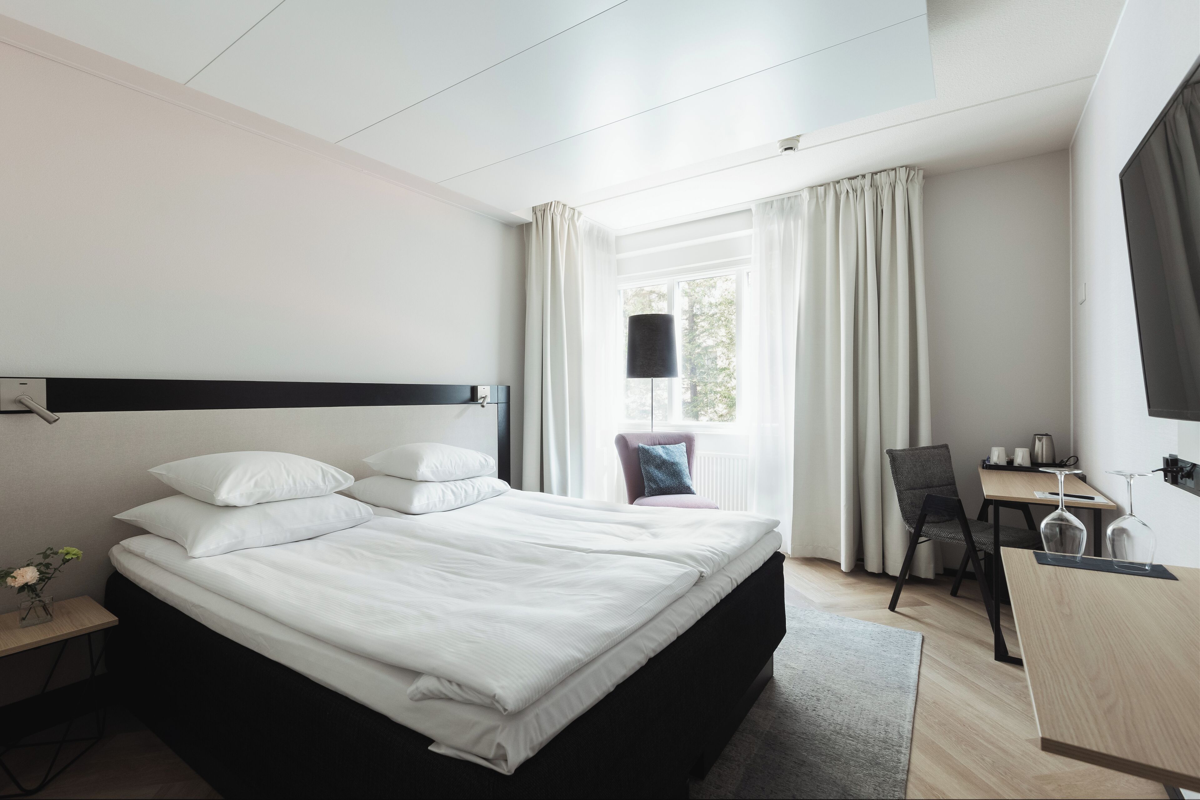 A modern hotel room with a large bed, a desk, and a chair.