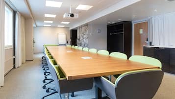 Un salón de conferencias con una larga mesa, sillas, un proyector, una pizarra y un reloj en la pared.