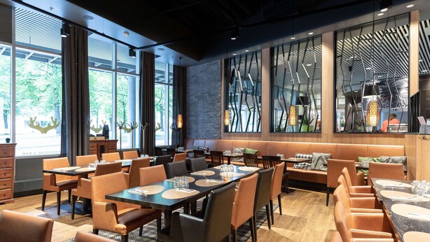 Un restaurant moderne avec des tables et des chaises hautes, de grandes fenêtres et une vue sur l’extérieur.