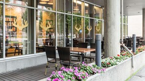 Un espace extérieur aménagé avec des tables et des chaises, un bac en béton orné de fleurs et un bâtiment doté de grandes fenêtres sur lesquelles est affiché un panneau indiquant un restaurant.