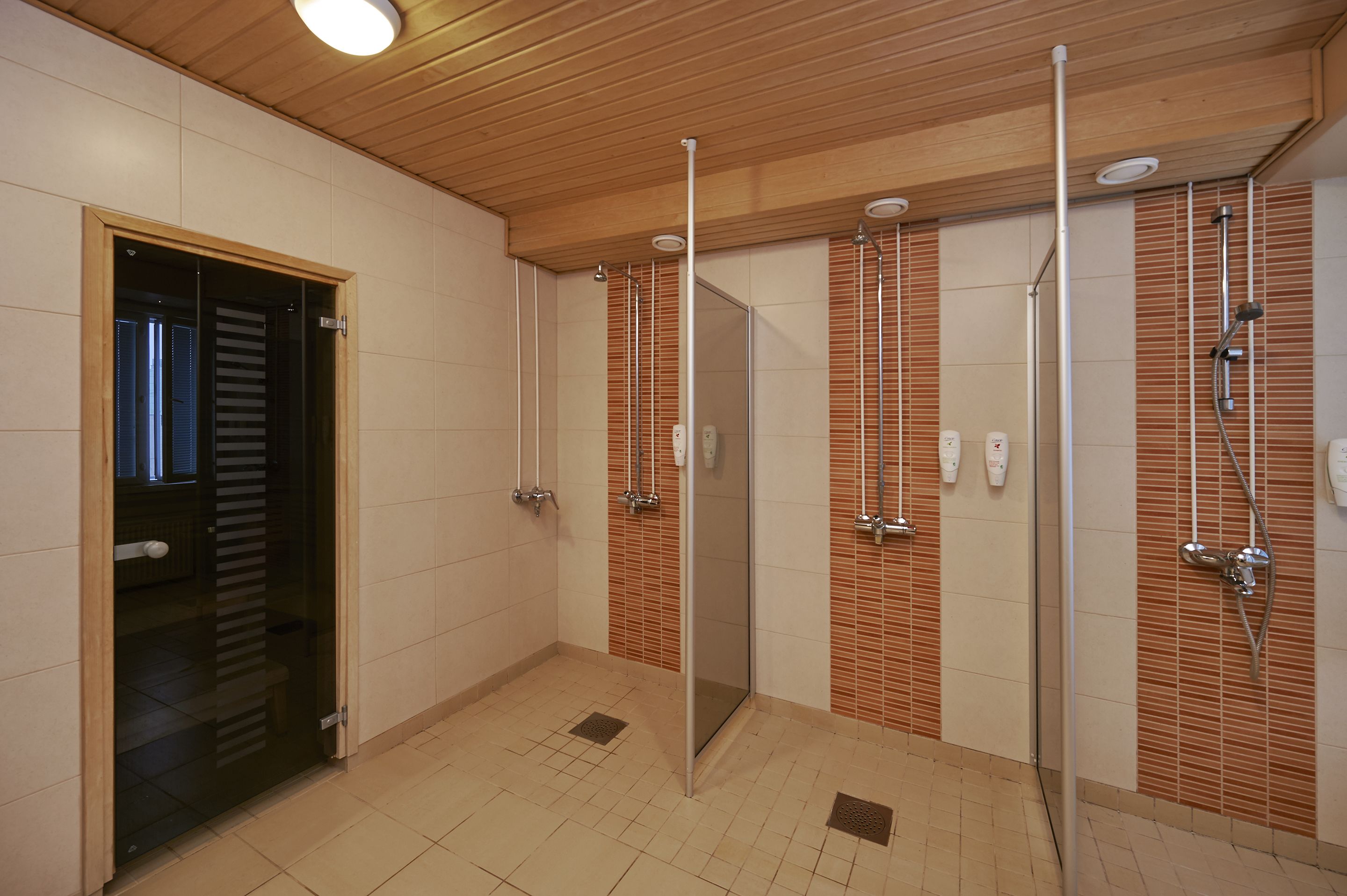 Een moderne badkamer met een houten plafond, betegelde wanden en een glazen douchecabine.