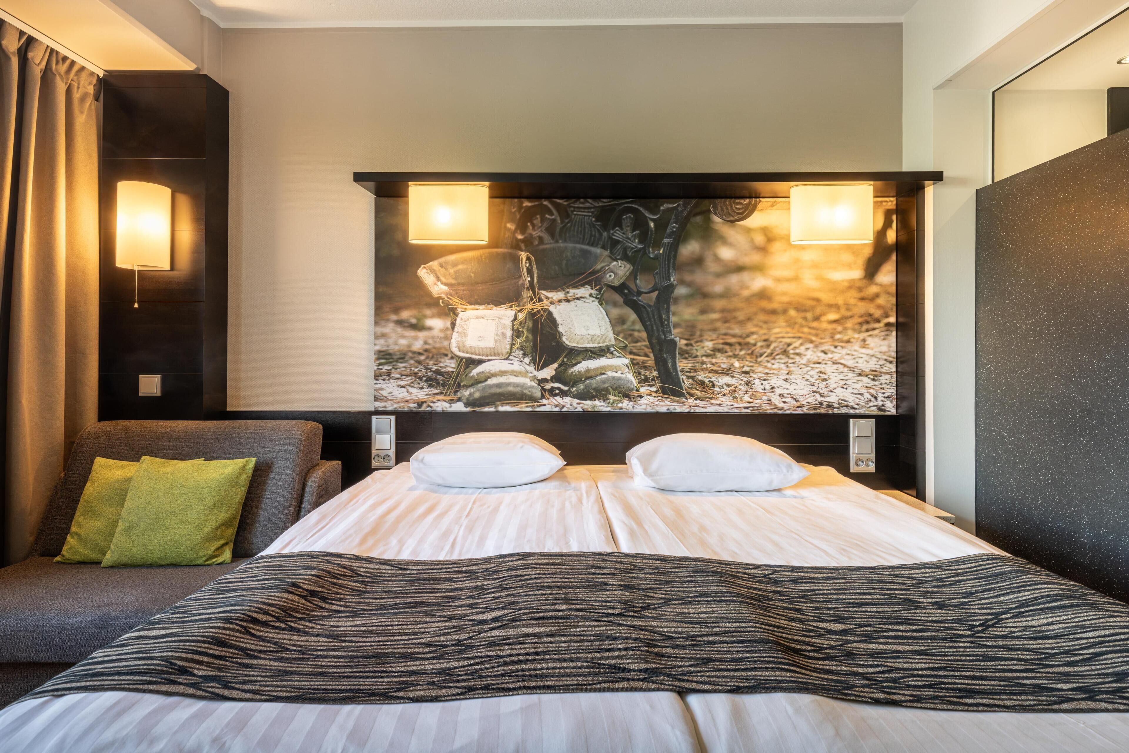 A hotel room with a bed, two bedside lamps, a wall-mounted TV, and a view of a rocky landscape.
