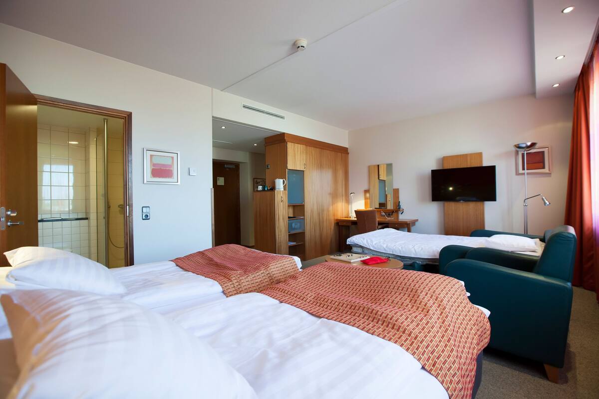 A hotel room with two beds, a desk with a chair, a television, and a bathroom visible through an open door.