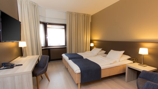 A hotel room with a bed, desk, and chairs. - Hotel Oscar (Varkaus)